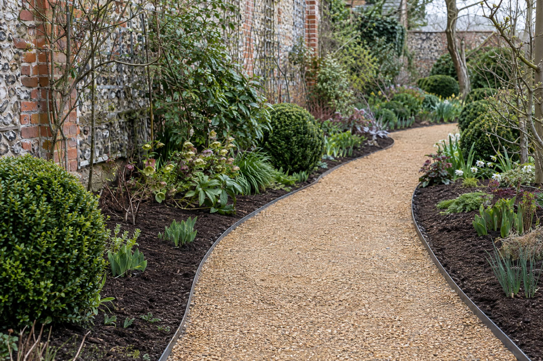 Freshly laid gravel path curving through a mulched border, with steel edging holding a clean line