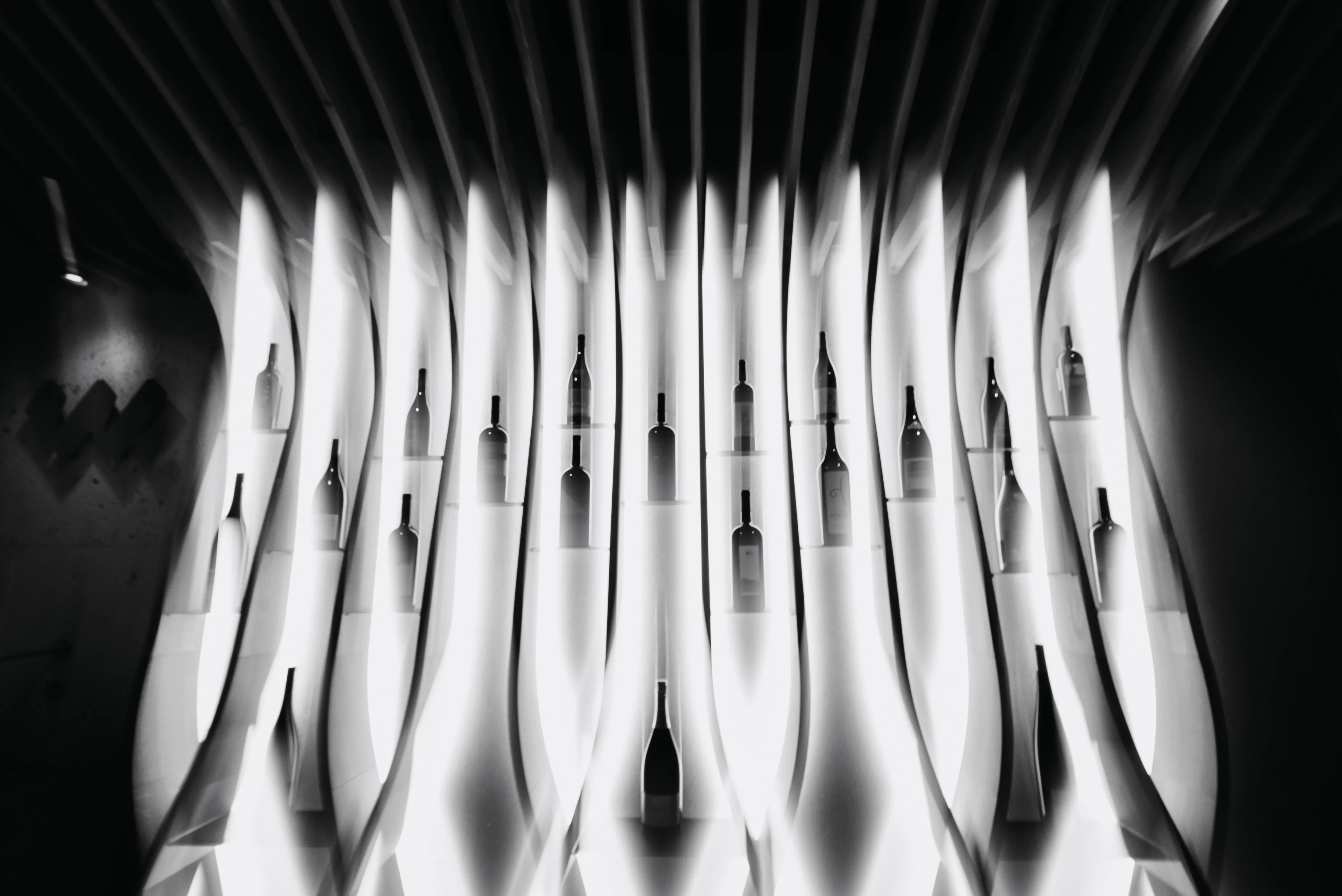 Artistic black and white display of wine bottles on illuminated wavy vertical panels.