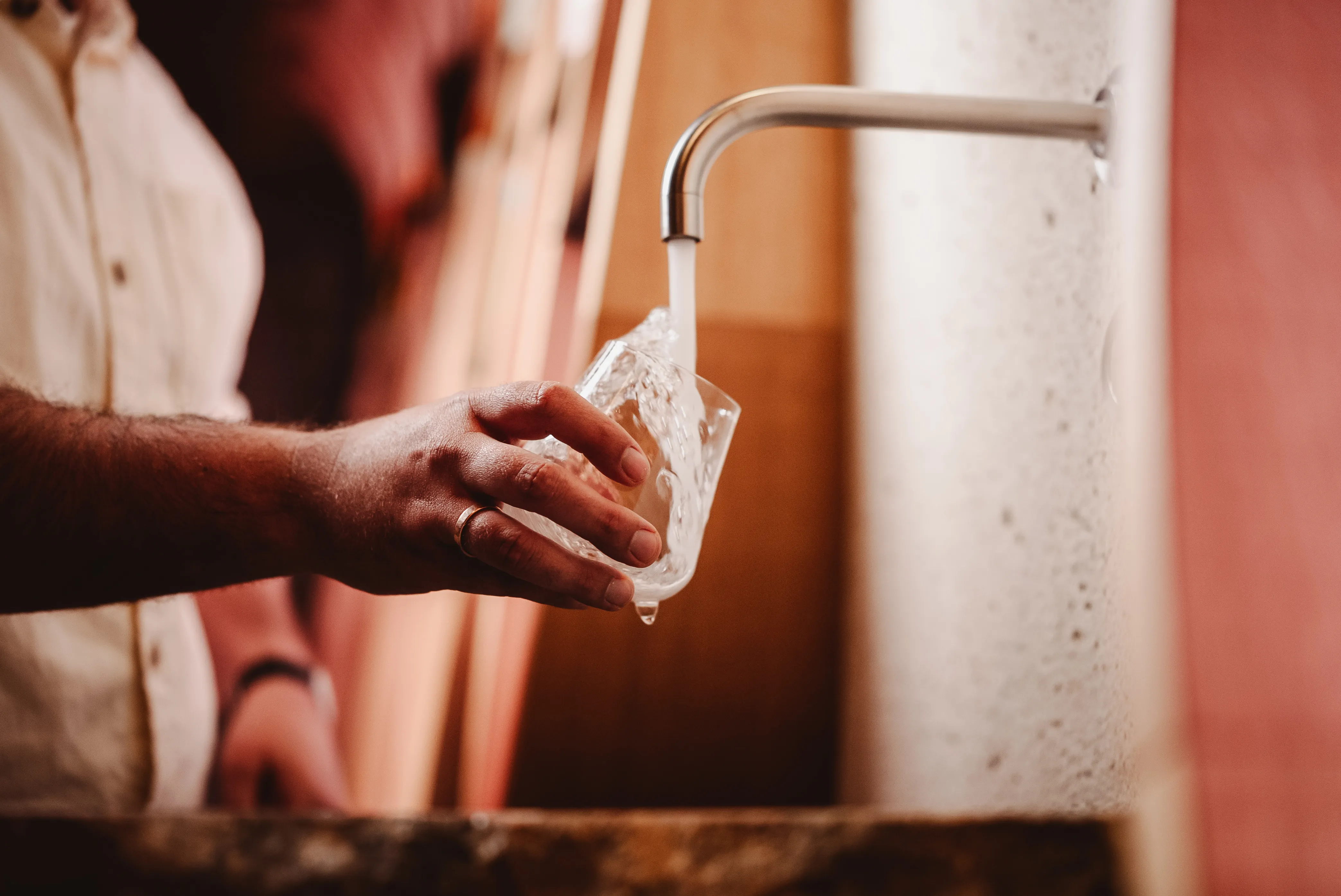 Hand with wedding ring filling a glass with water from a metal faucet.