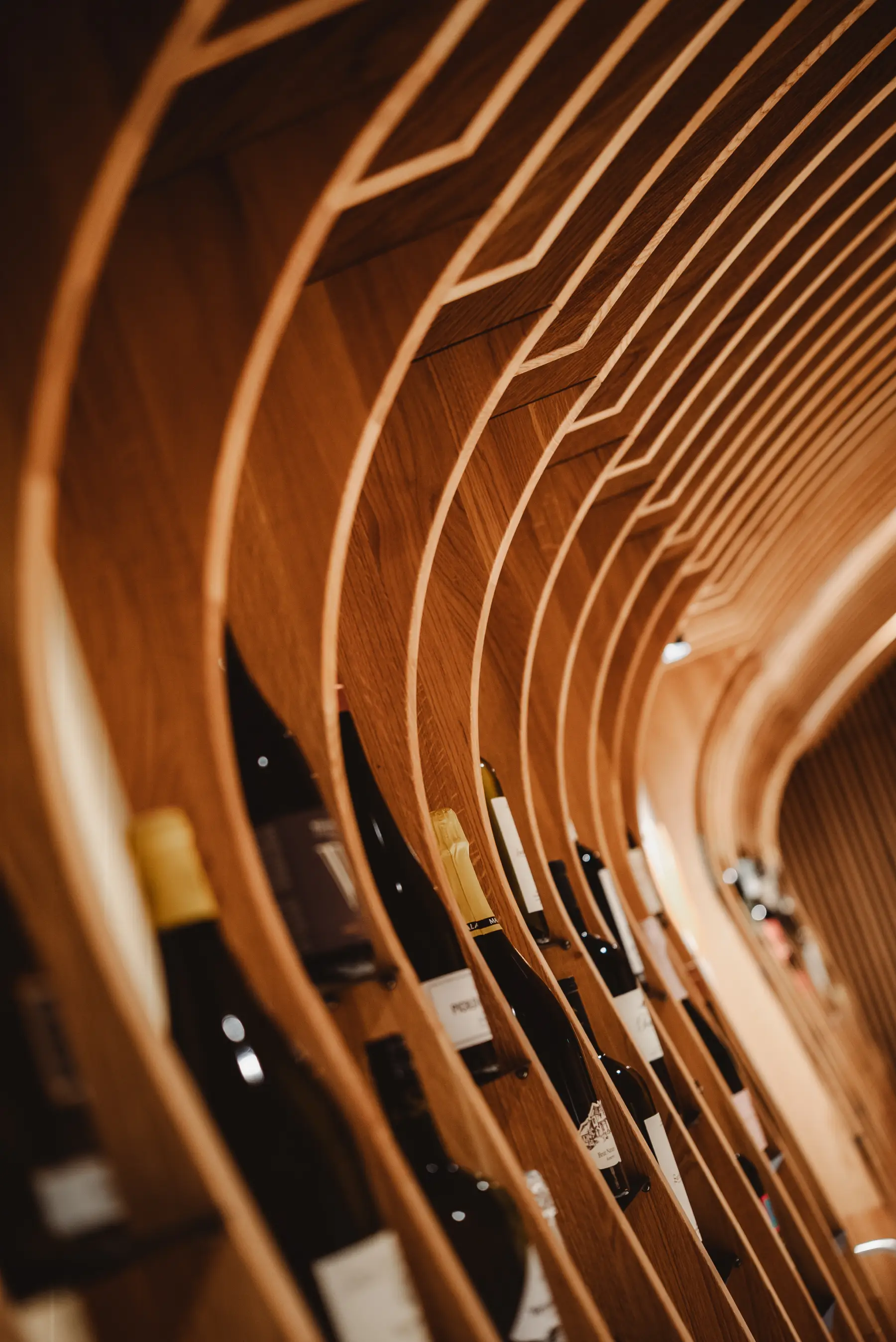 Curved wooden wine rack holding multiple wine bottles stored horizontally.