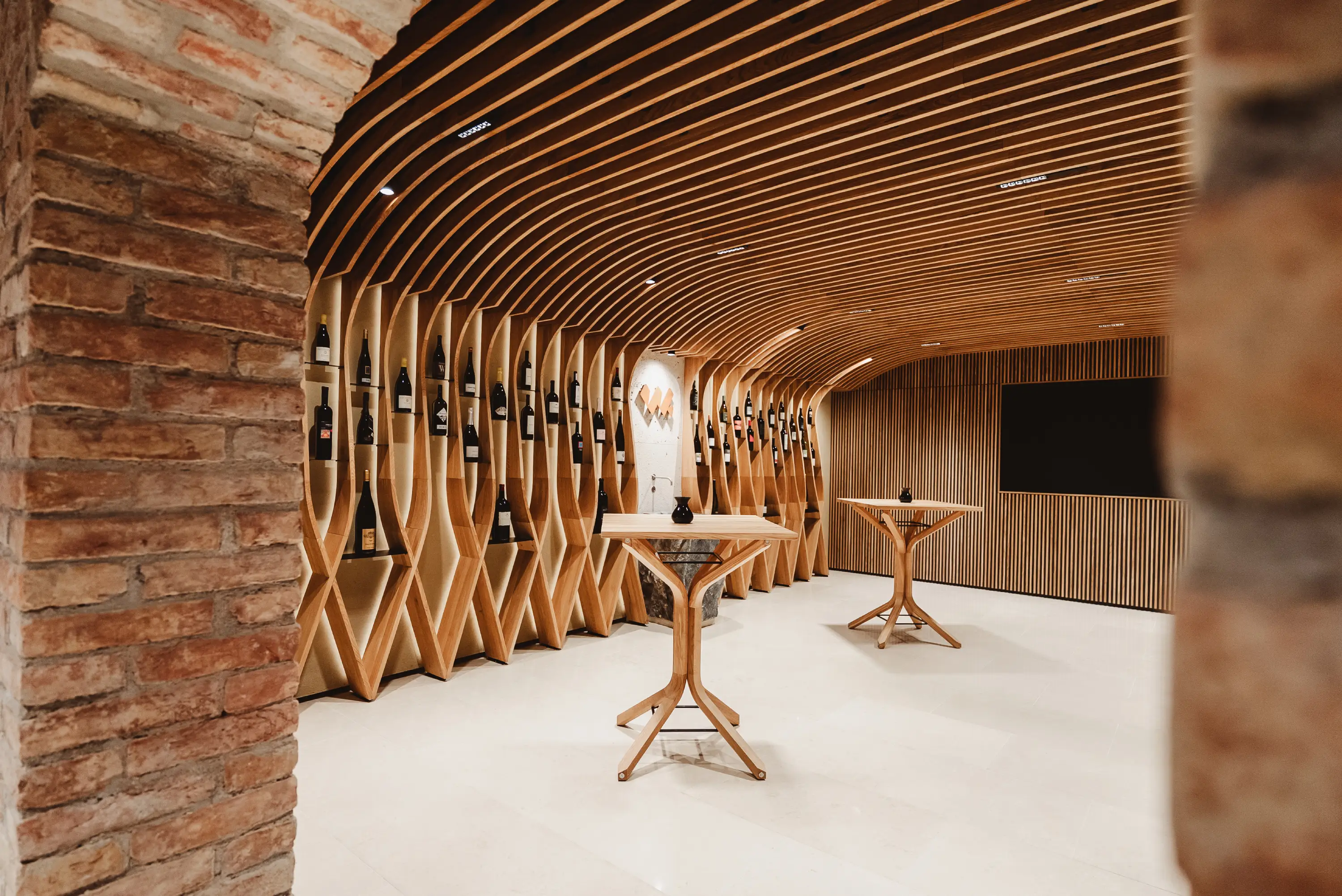 Modern wine tasting room with wooden shelves holding wine bottles and two standing tables.