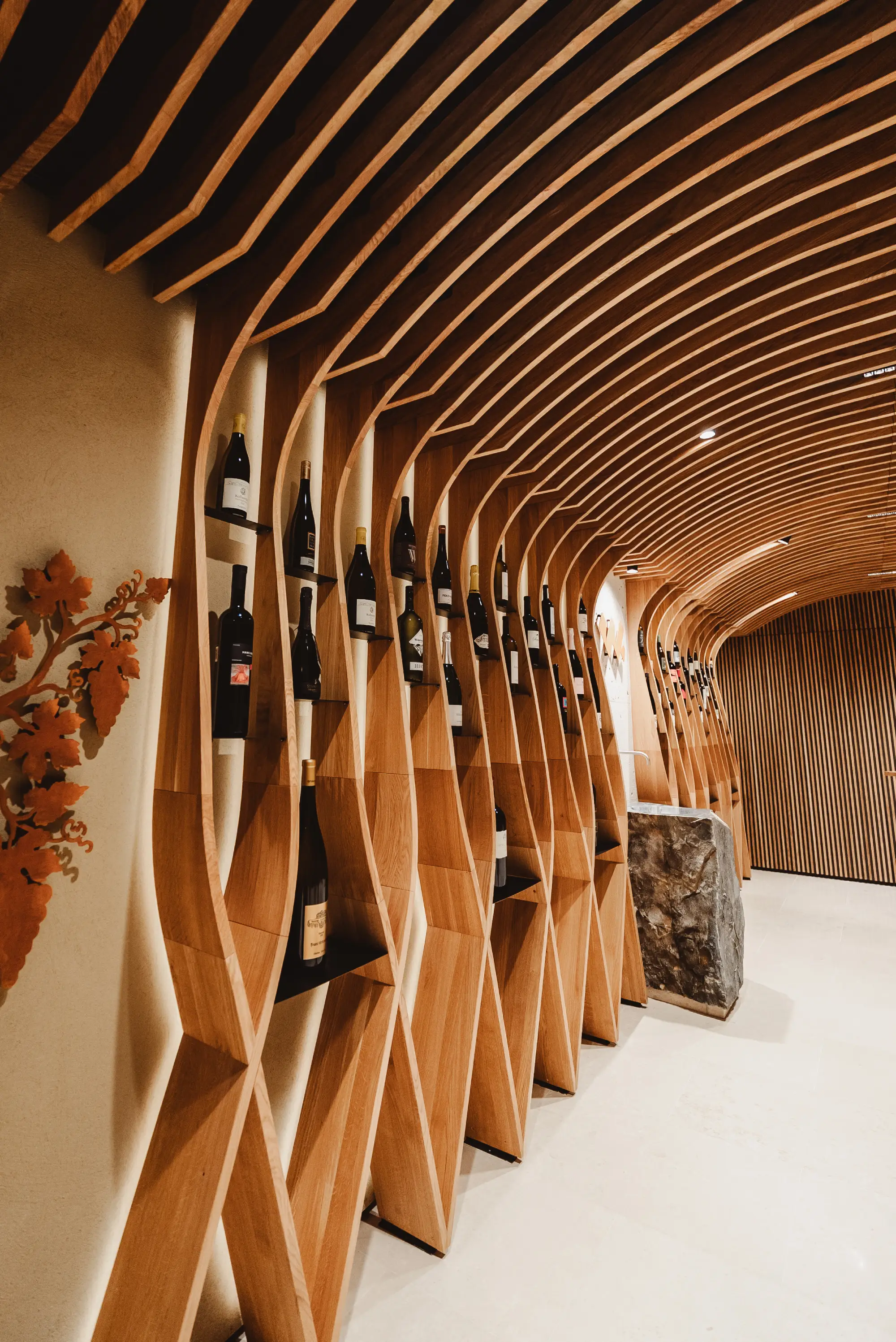 Modern wine cellar with curved wooden racks holding bottles and a stone counter.