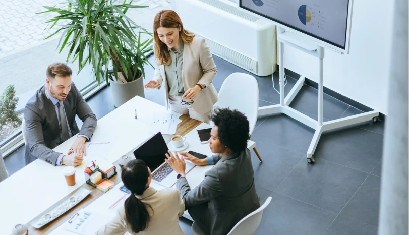 Four businesspeople in a meeting discussing charts with a laptop and coffee on a white table.