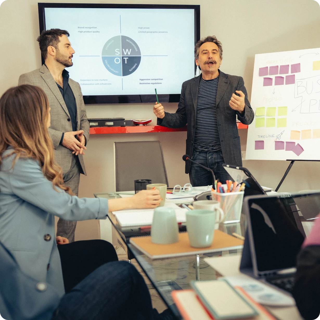 Man presenting SWOT analysis on screen while team listens during a business meeting in an office.