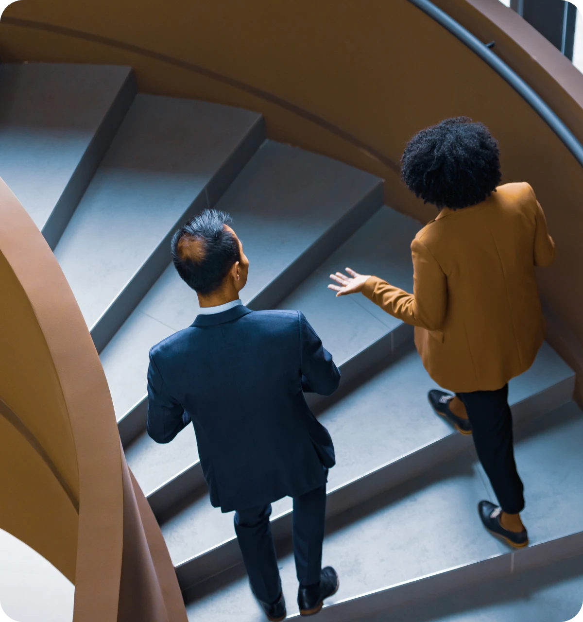 Two office workers walking up a curved staircase inside a modern building.