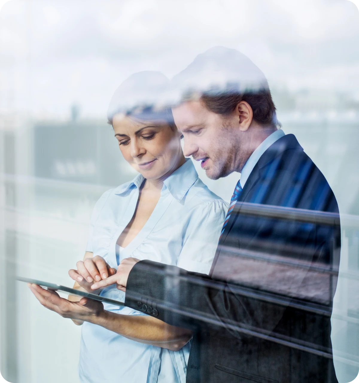 Two coworkers looking at a tablet, discussing work with reflections on glass window.