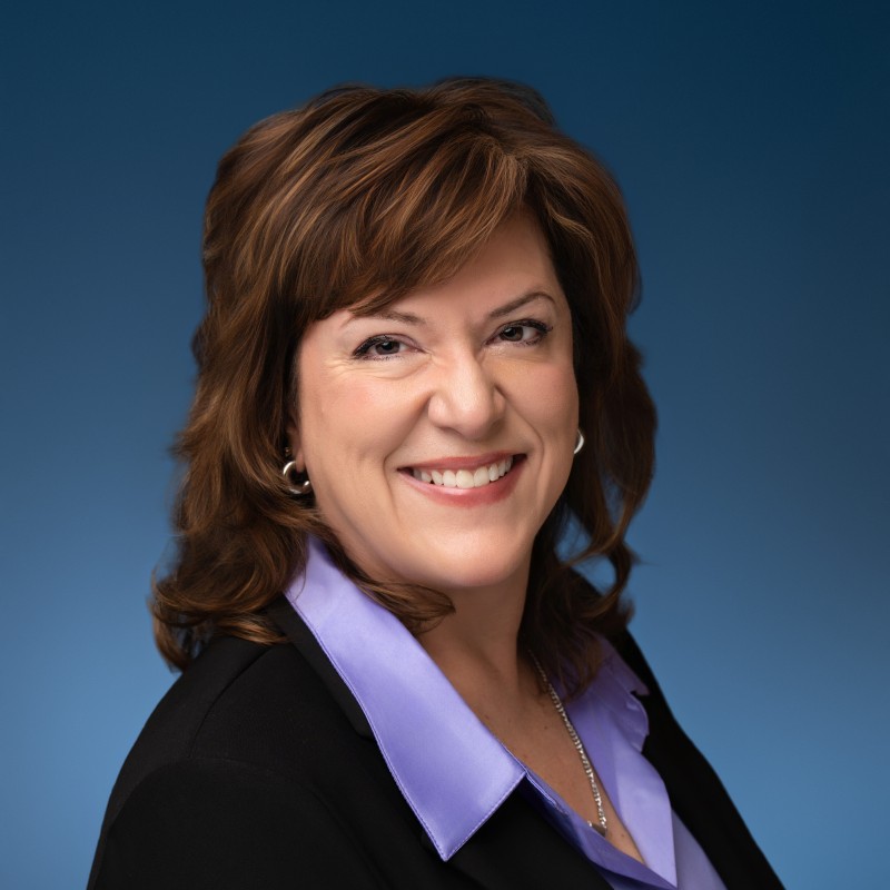 Smiling woman with shoulder-length brown hair wearing a black blazer and lavender collared shirt.