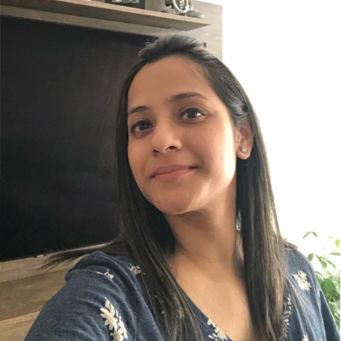 Woman with long dark hair wearing a blue top with white floral patterns, smiling softly indoors.