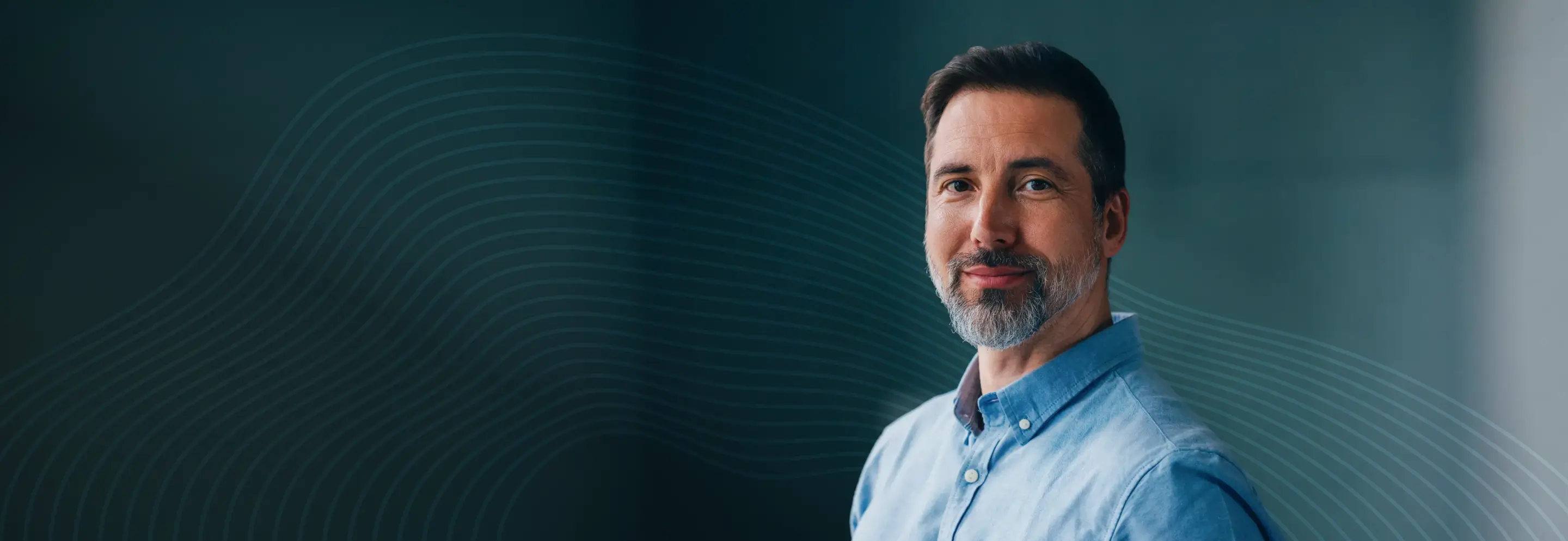 Smiling middle-aged man with beard wearing a blue button-up shirt on dark background with wave lines.