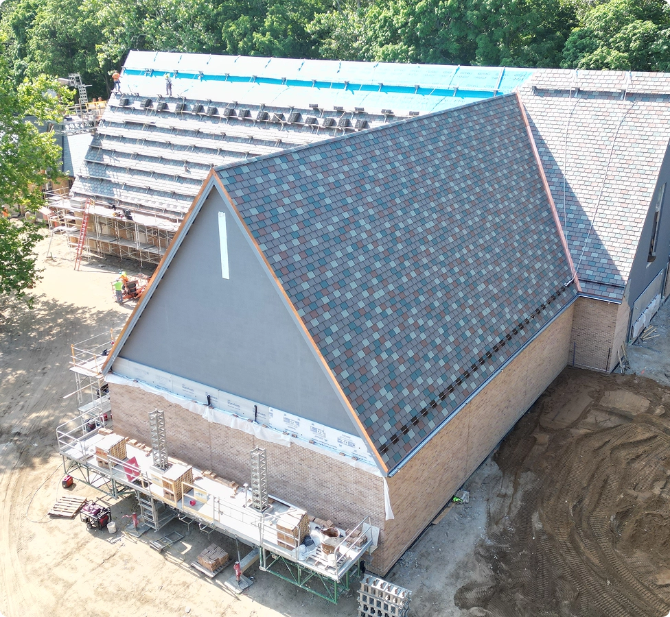 Aerial view of a building under construction with a new tiled roof and scaffolding on one side.
