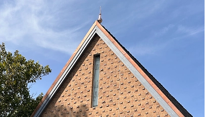 The top of the HARC building with narrow vertical window framed by blue sky and tree branches.