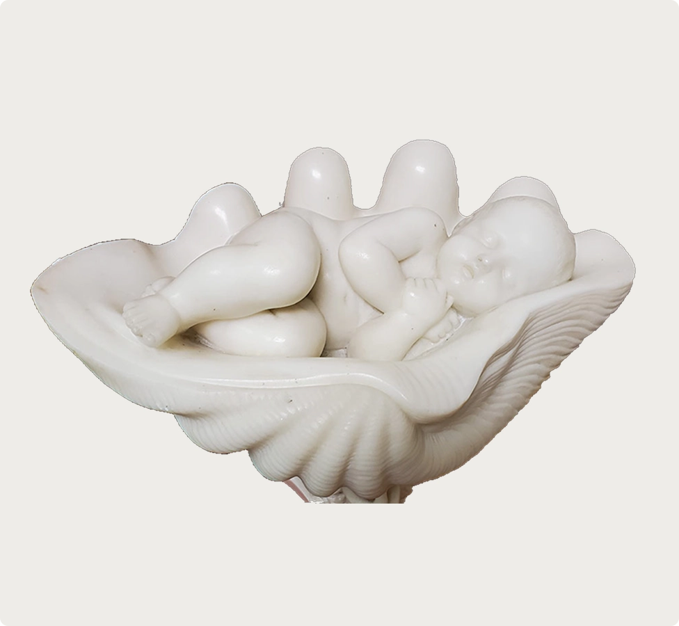 White sculpture of a sleeping baby lying curled up inside a large seashell.