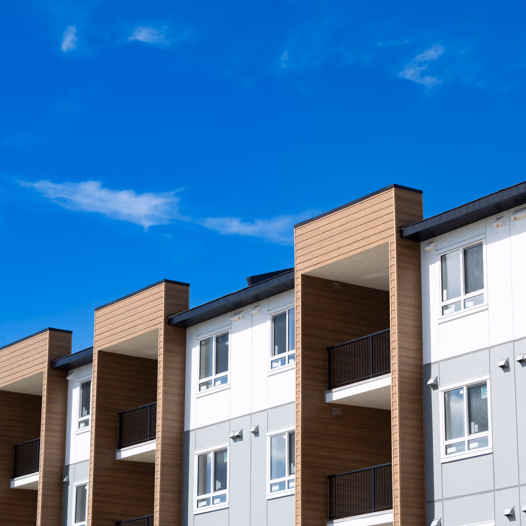 Modern multi-story apartment building with balconies under a blue sky.