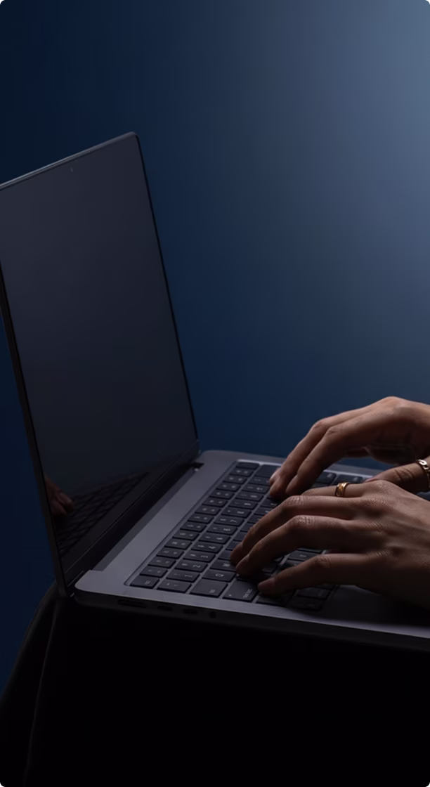Close-up of hands typing on a laptop keyboard with a dark screen and blue background.