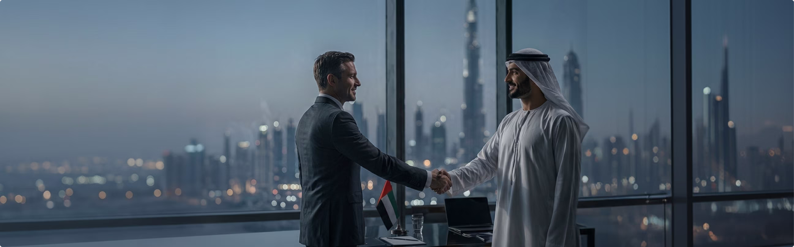 Two businessmen shaking hands in an office with a city skyline and a UAE flag in the background.