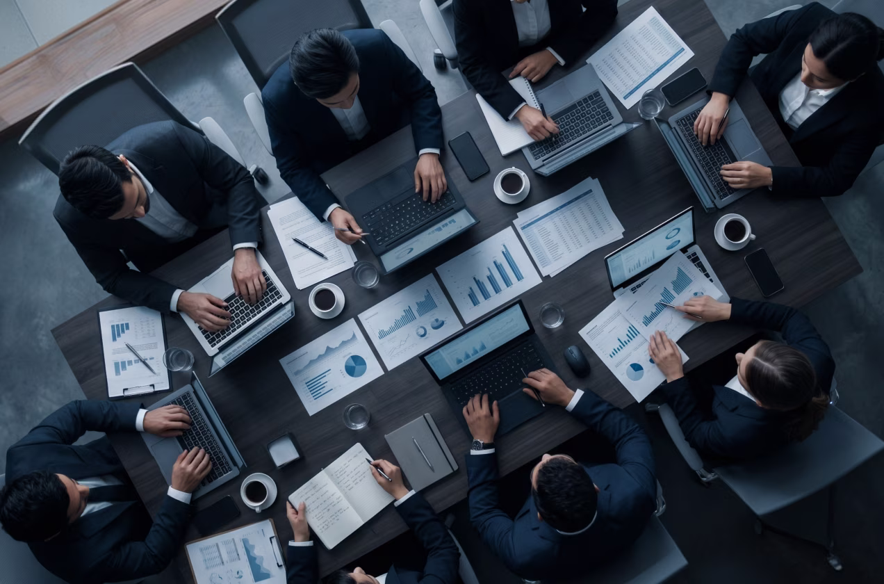 Business team in suits working on laptops and analyzing charts around a meeting table.