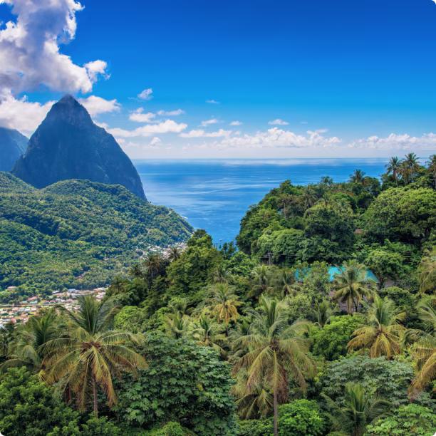 Lush green mountains and palm trees overlooking blue sea under a partly cloudy sky.