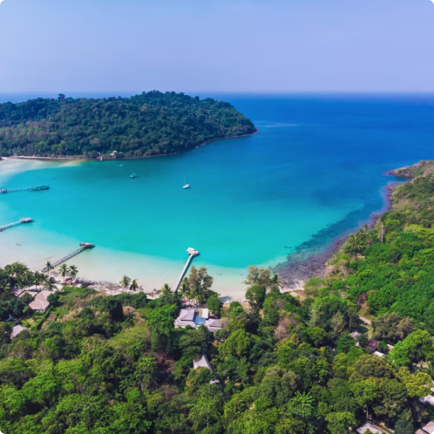 Aerial view of a tropical bay with turquoise waters, sandy beaches, piers, and lush green forest.