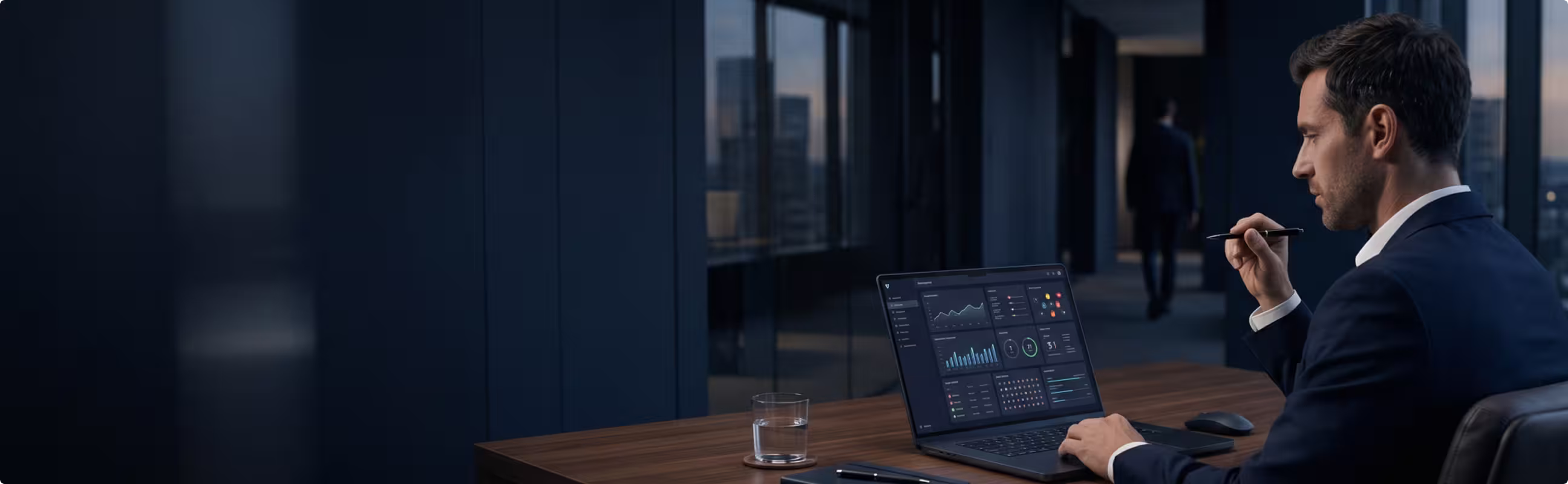 Businessman in suit working on laptop with data charts in a modern office with glass windows.