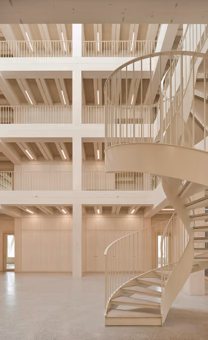 Mehrgeschossiger Innenraum in Holzbauweise mit offenen Galerieebenen und einer hellen Wendeltreppe.