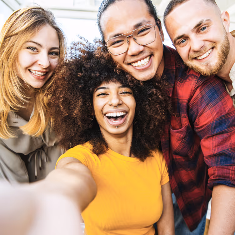Quatre jeunes adultes souriants prennent un selfie, montrant la diversité et la joie.