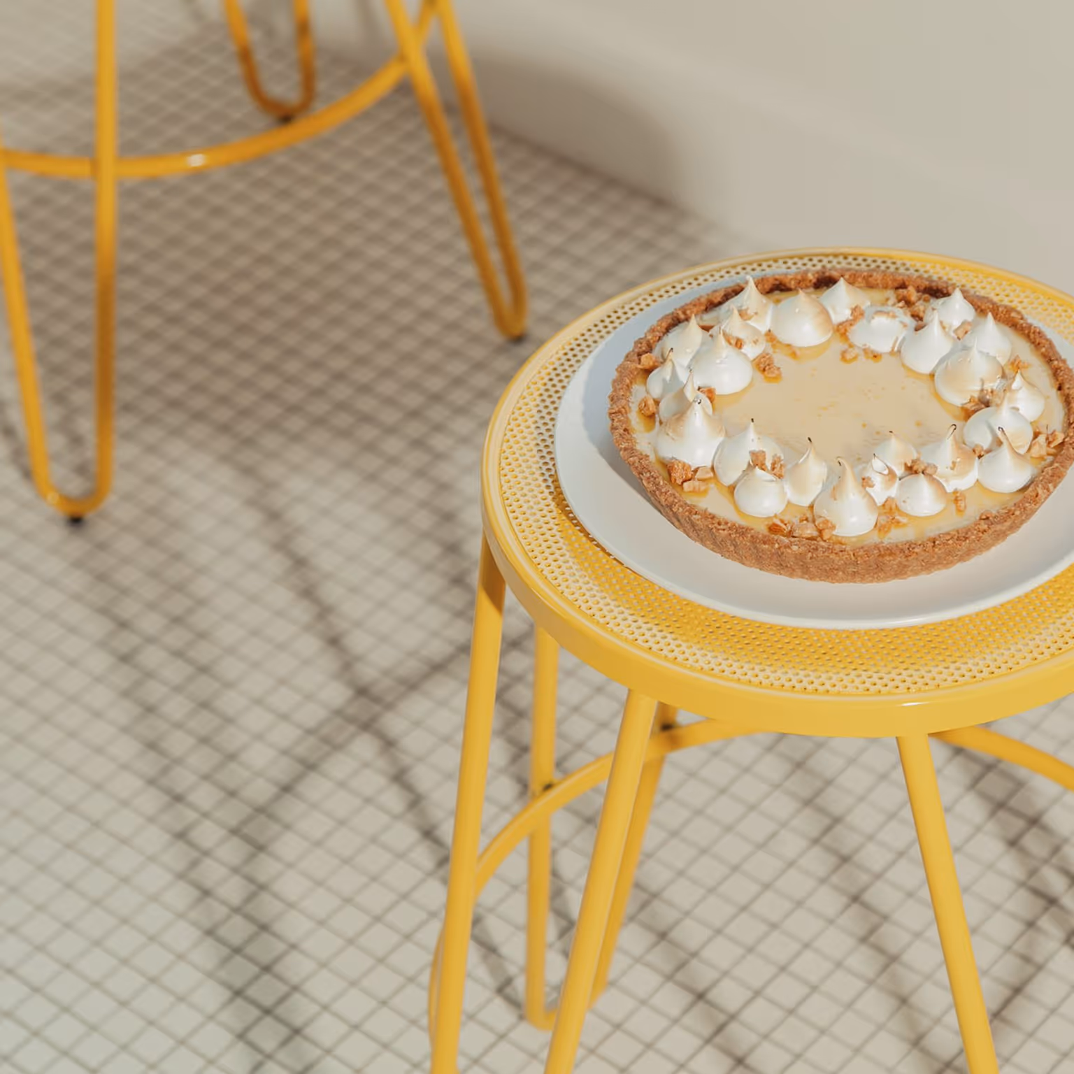 Tarte au citron meringuée sur une assiette blanche posée sur une table ronde jaune.