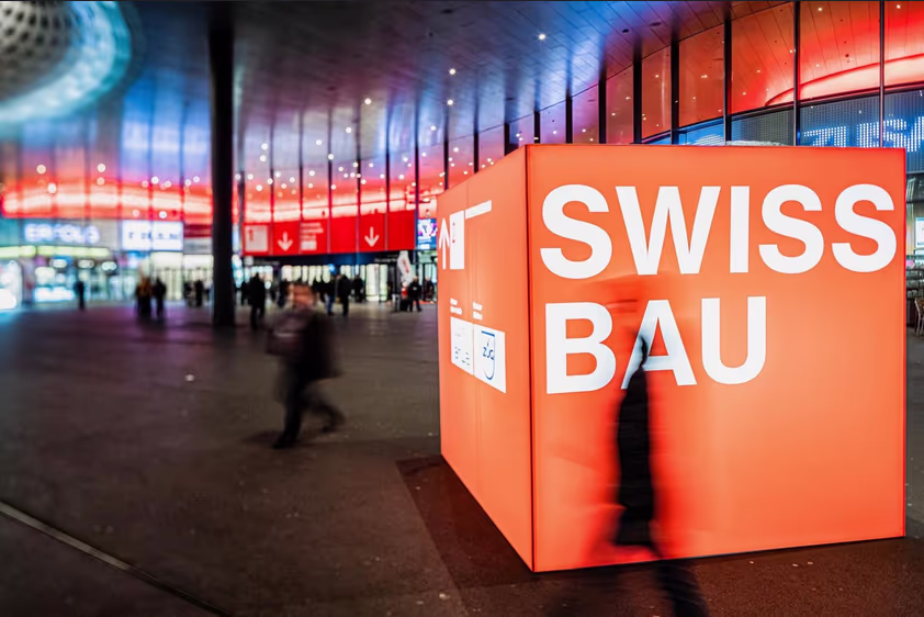 Un gros cube rouge sur lequel est dessiné le logo de Swissbau est posé dans un grans espace public