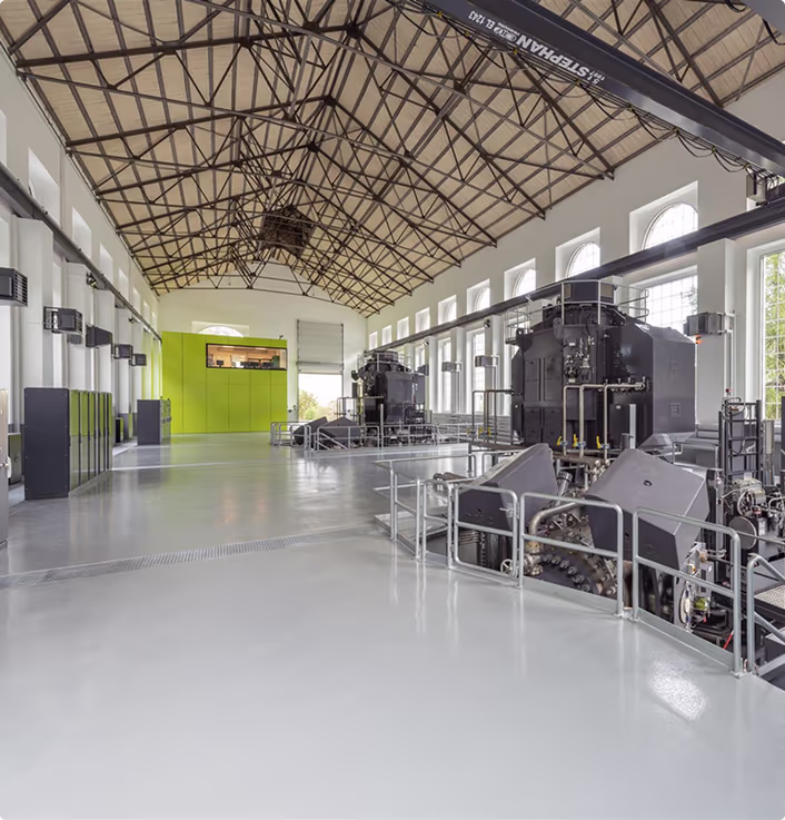 Intérieur d'une usine hydroélectrique récemment rénovée, des poutres métalliques sont exposées au plafond et des machines sortent du sol
