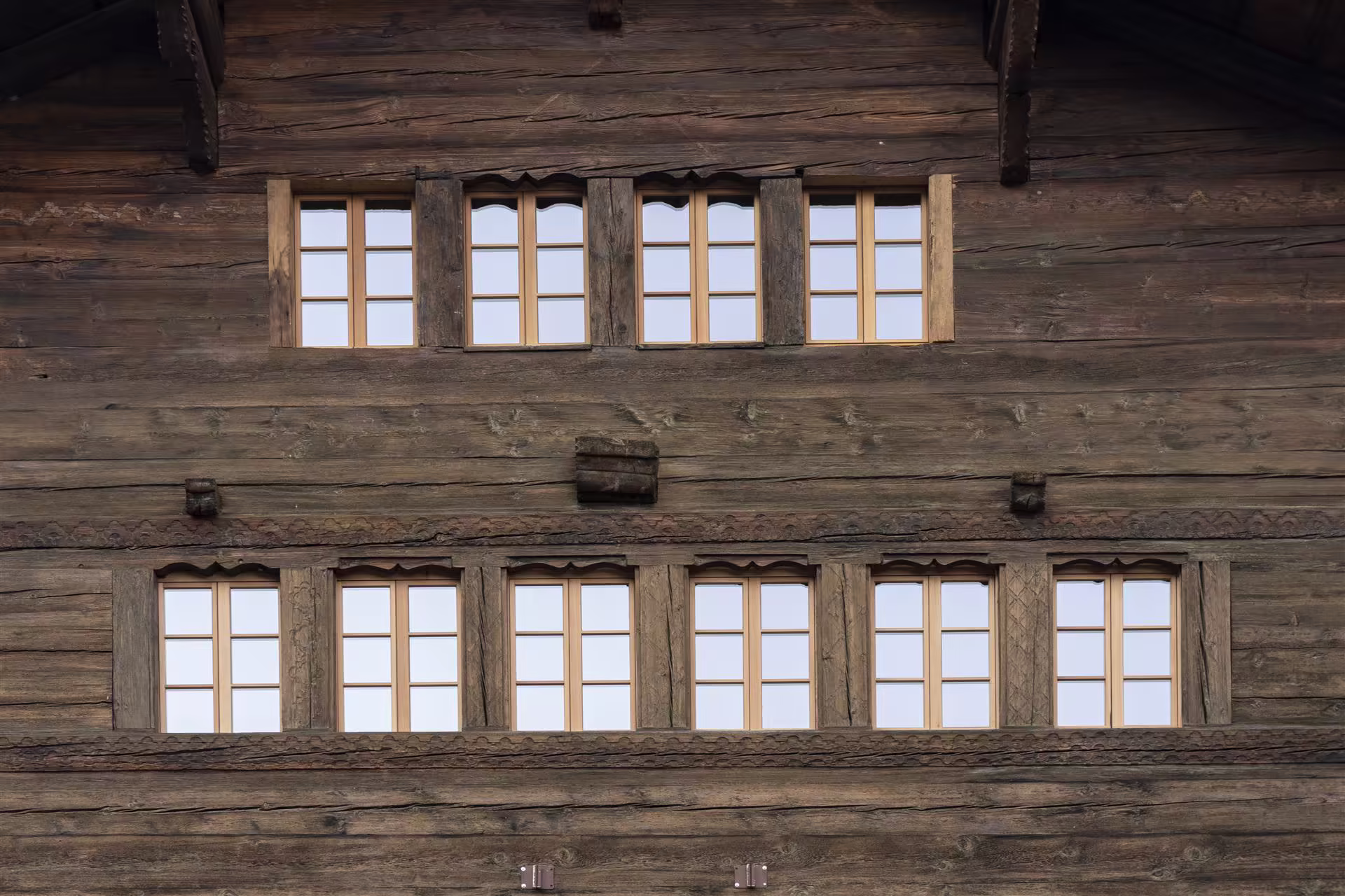 Façade en bois foncé avec deux rangées de fenêtres à petits carreaux, six en bas et quatre en haut, encadrées de bois sculpté.