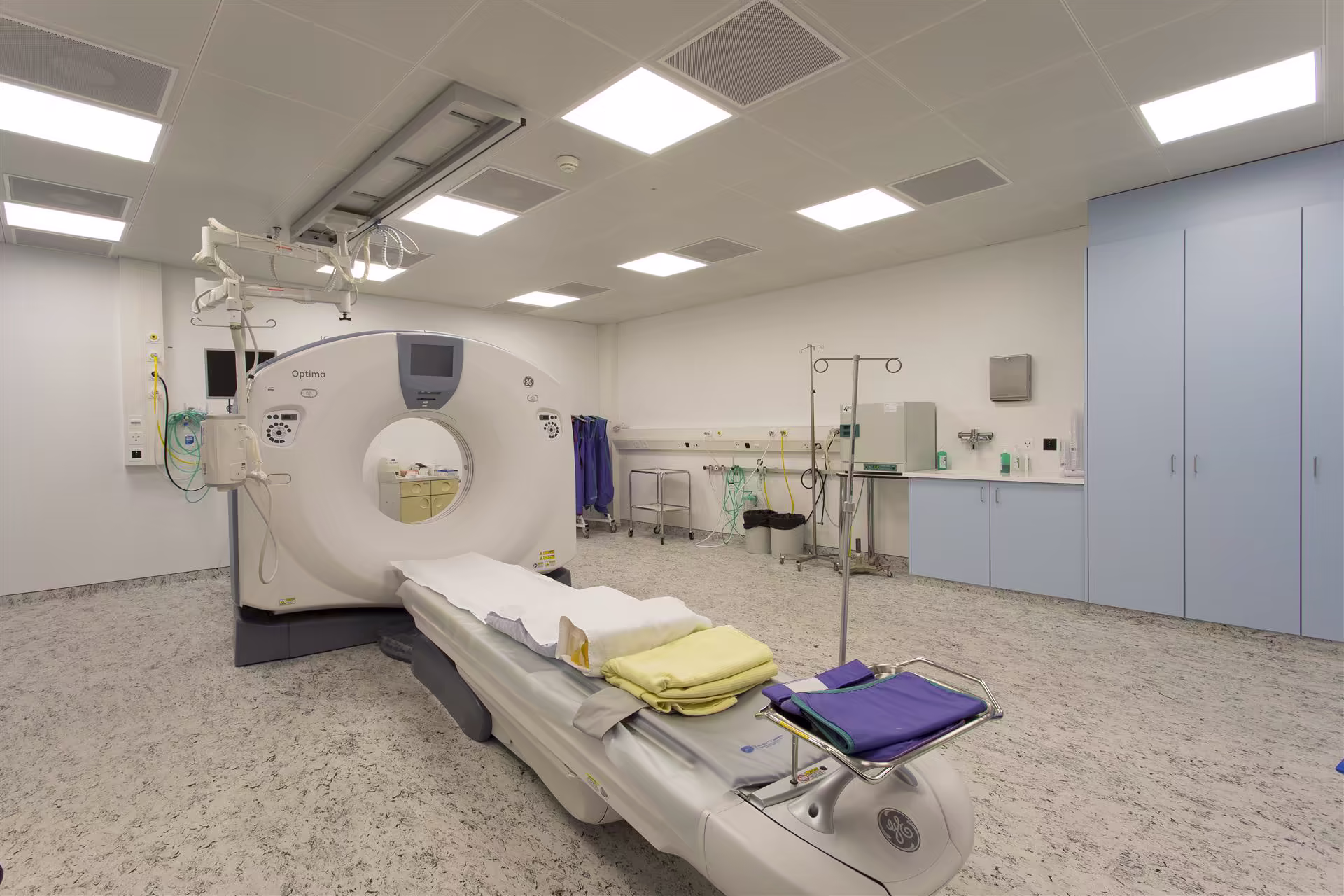 Salle d’imagerie médicale équipée d’un scanner, table d’examen avec draps, et divers équipements médicaux dans un environnement propre et éclairé.