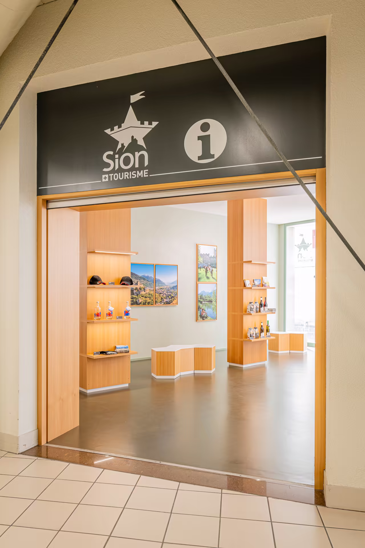 Entrée de l'office de tourisme de Sion avec des présentoirs en bois, des souvenirs exposés et des photos de paysages montagnards aux murs.