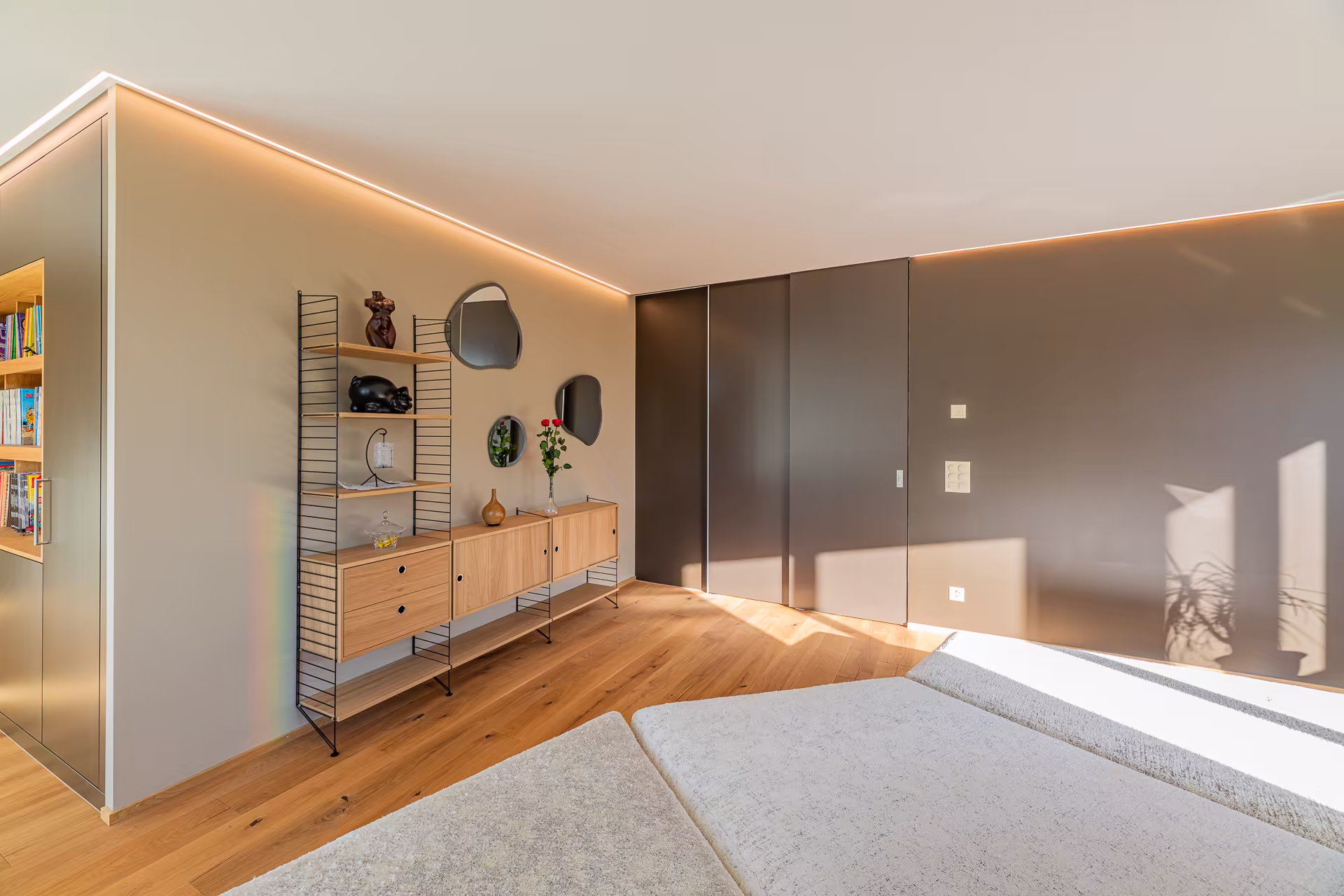 Chambre moderne avec parquet, commode suspendue en bois clair, miroirs muraux irréguliers et lumière naturelle filtrée par une grande fenêtre.