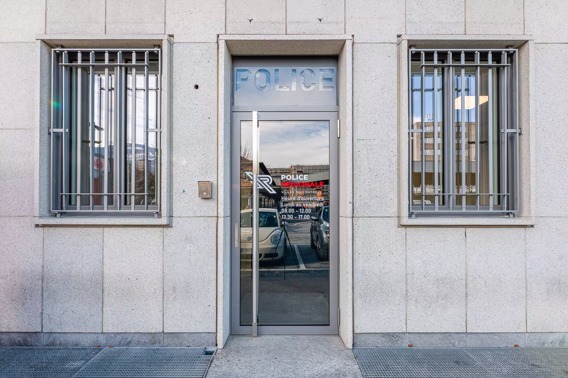 Façade en pierre claire avec porte en verre marquée "Police Régionale" et fenêtres à barreaux, battant des heures d'ouverture du lundi au vendredi.