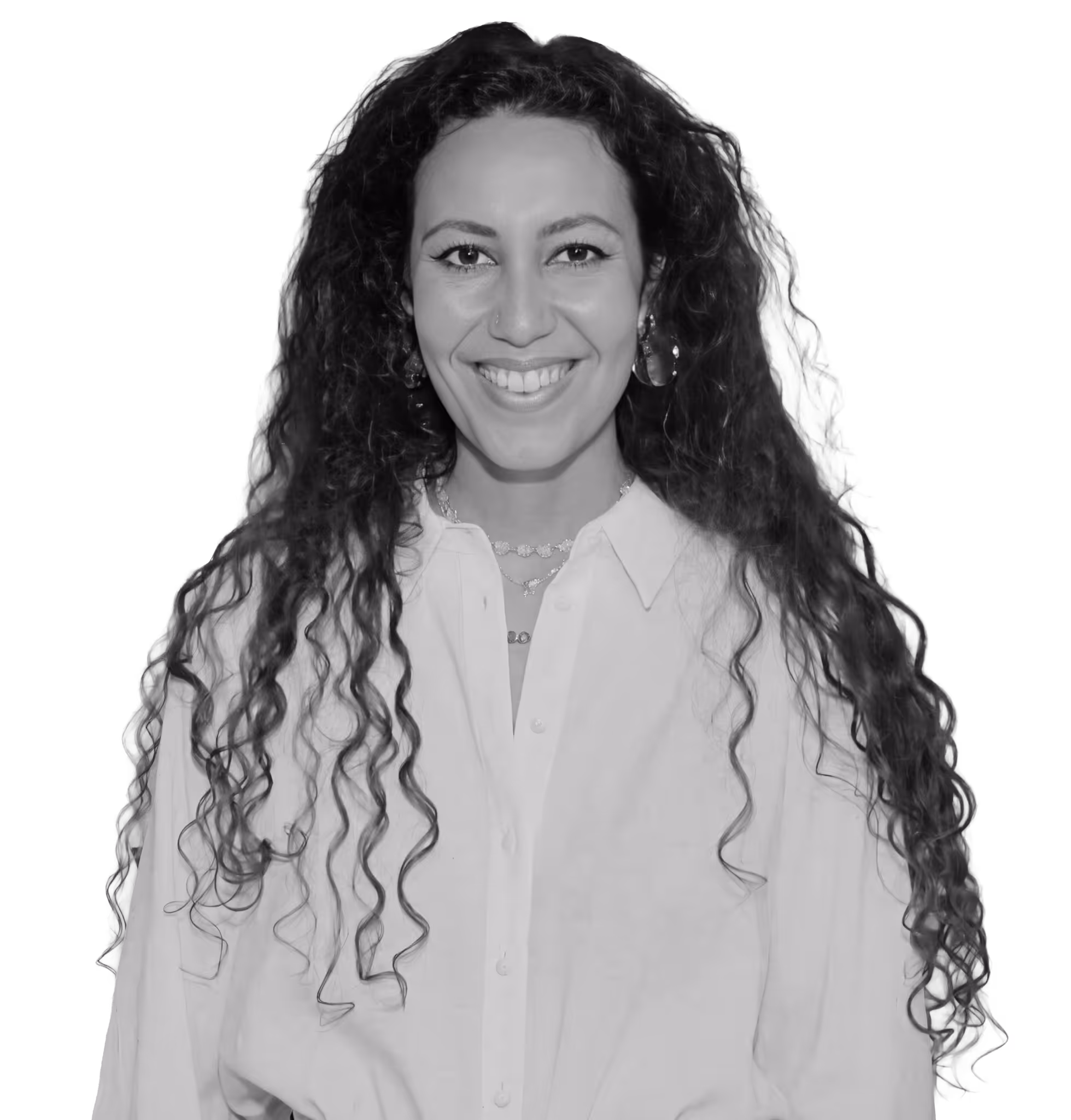 Mujer joven con cabello rizado oscuro, gafas y sonrisa amplia, vestida con camisa blanca y sobrepelliz negra.