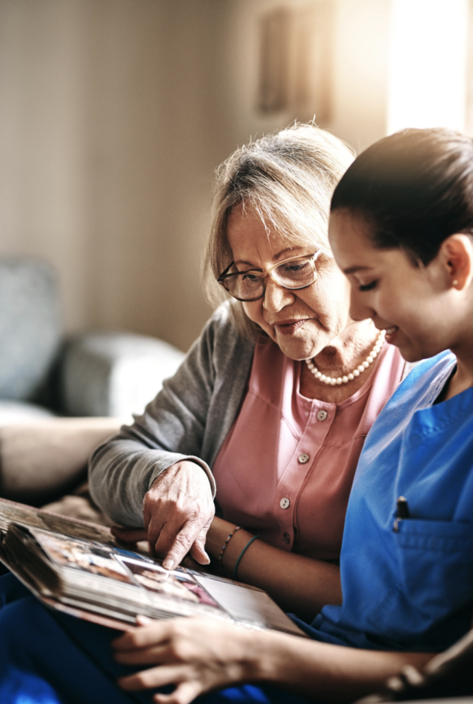 A carer and an older woman look through a photo album together