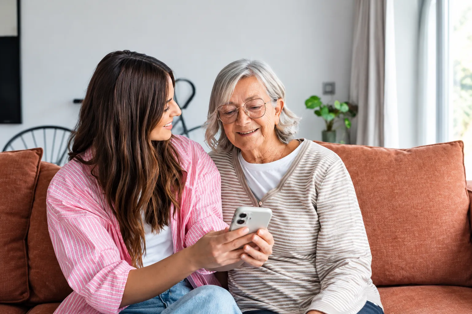 A young woman and her grandmother look at a phone together on a sofa