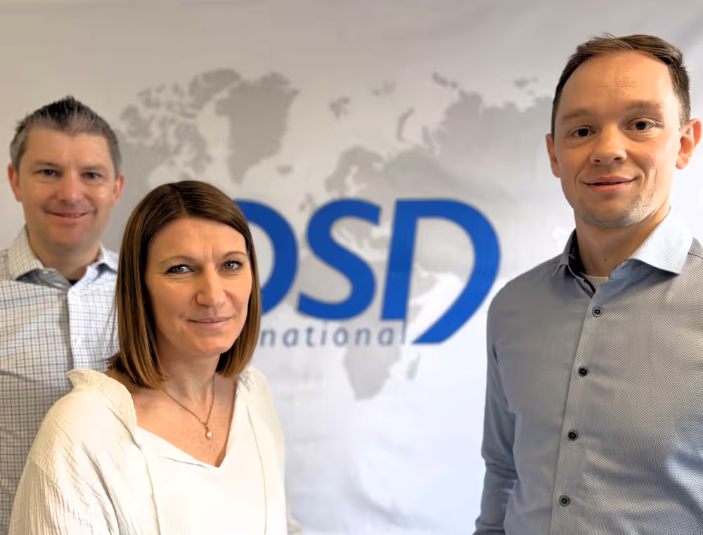 Three people standing in front of a wall with a blurred OSD International logo and world map.