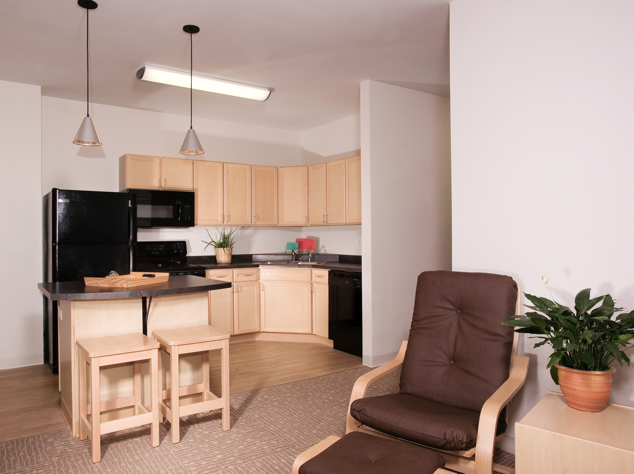 Living area with chair, and view of Kitchen with black appliances and breakfast bar with chairs