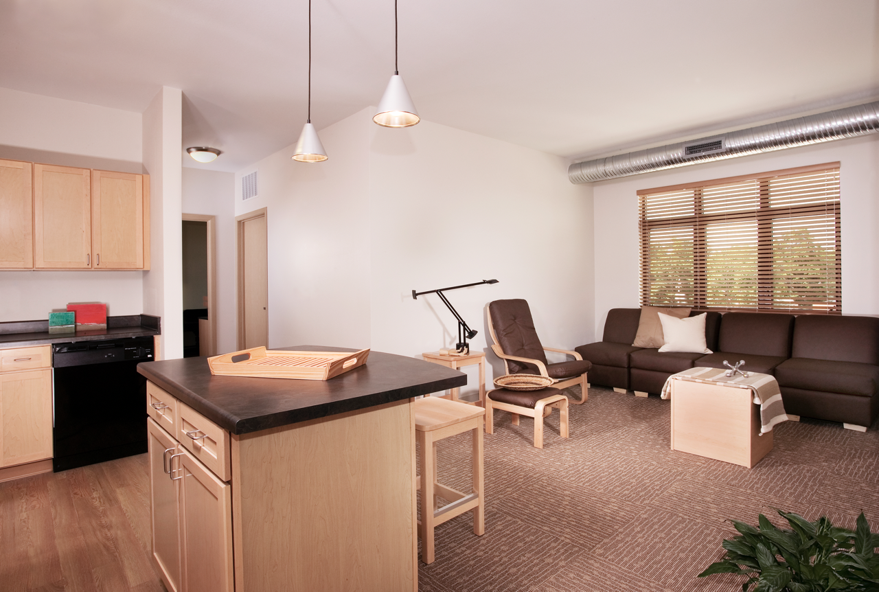 Living area with chair, and view of Kitchen with black appliances and breakfast bar with chairs
