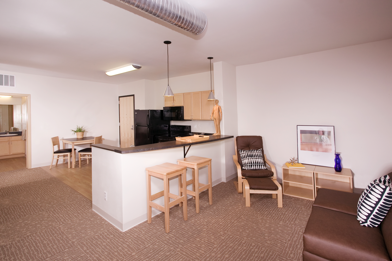 Living area with chair, and view of Kitchen with black appliances and breakfast bar with chairs