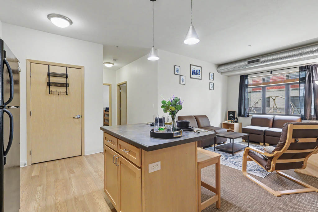 Living area with chair, and view of Kitchen with black appliances and breakfast bar with chairs