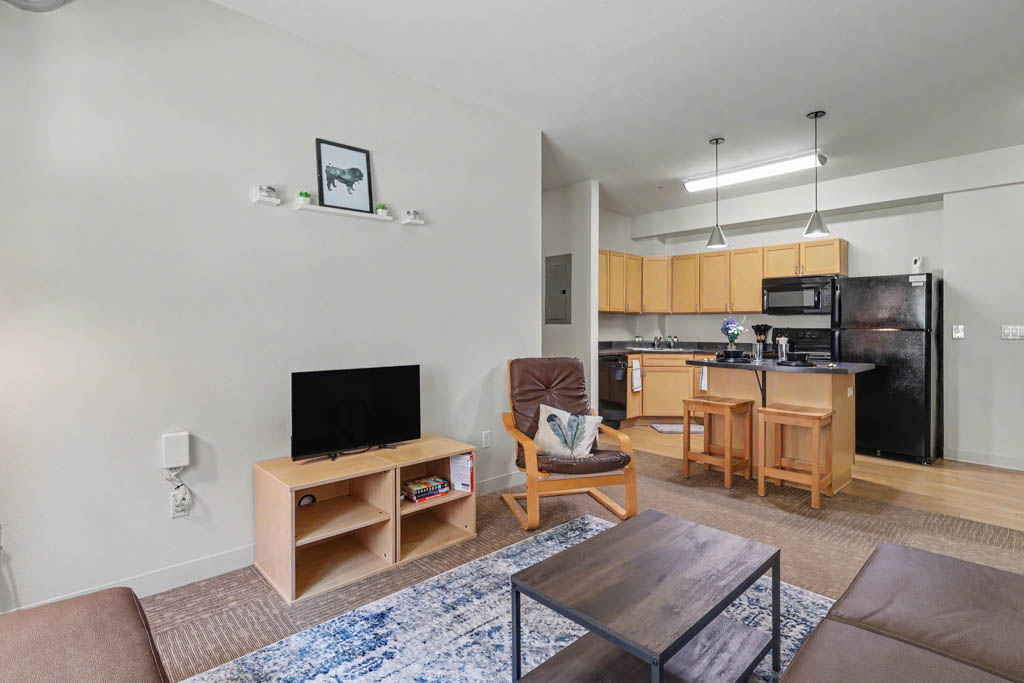 Living area with chair, and view of Kitchen with black appliances and breakfast bar with chairs