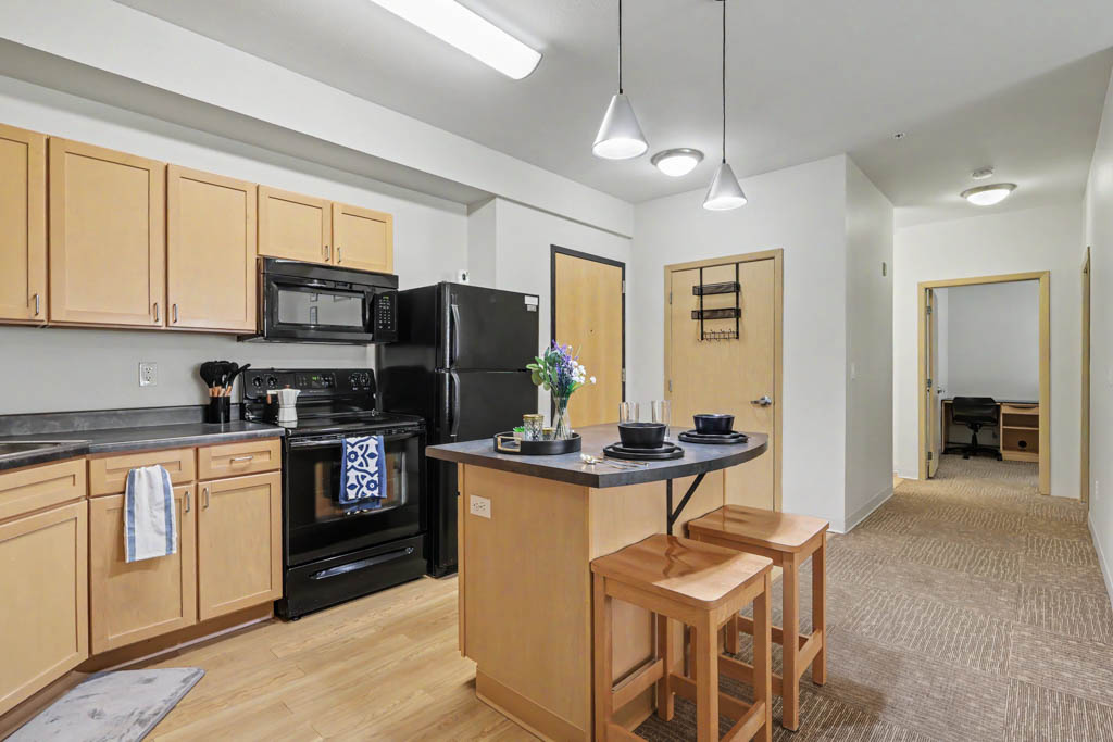 Living area with chair, and view of Kitchen with black appliances and breakfast bar with chairs