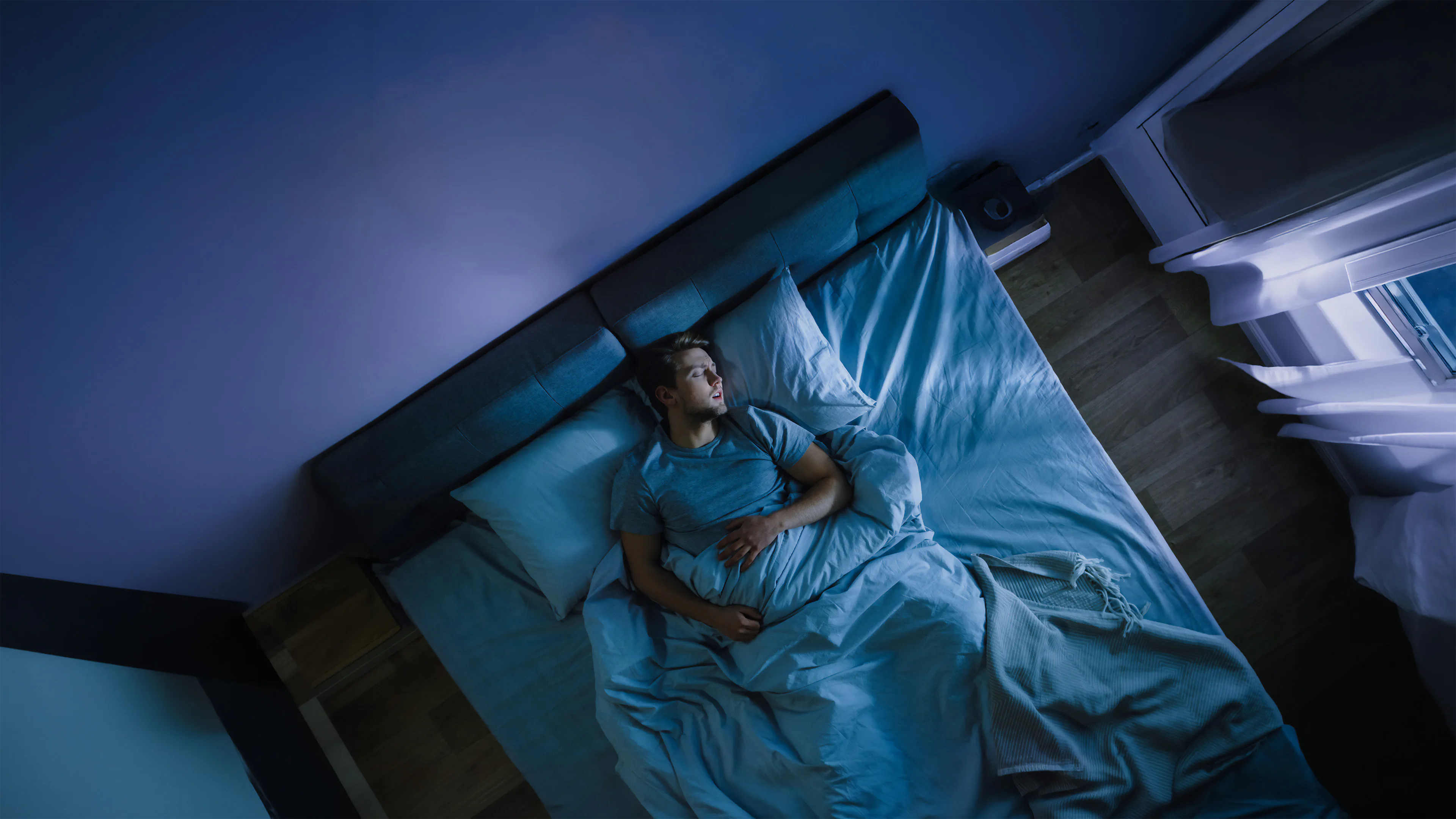 Man sleeping in bed at night, looking frustrated from sleep and airway problems