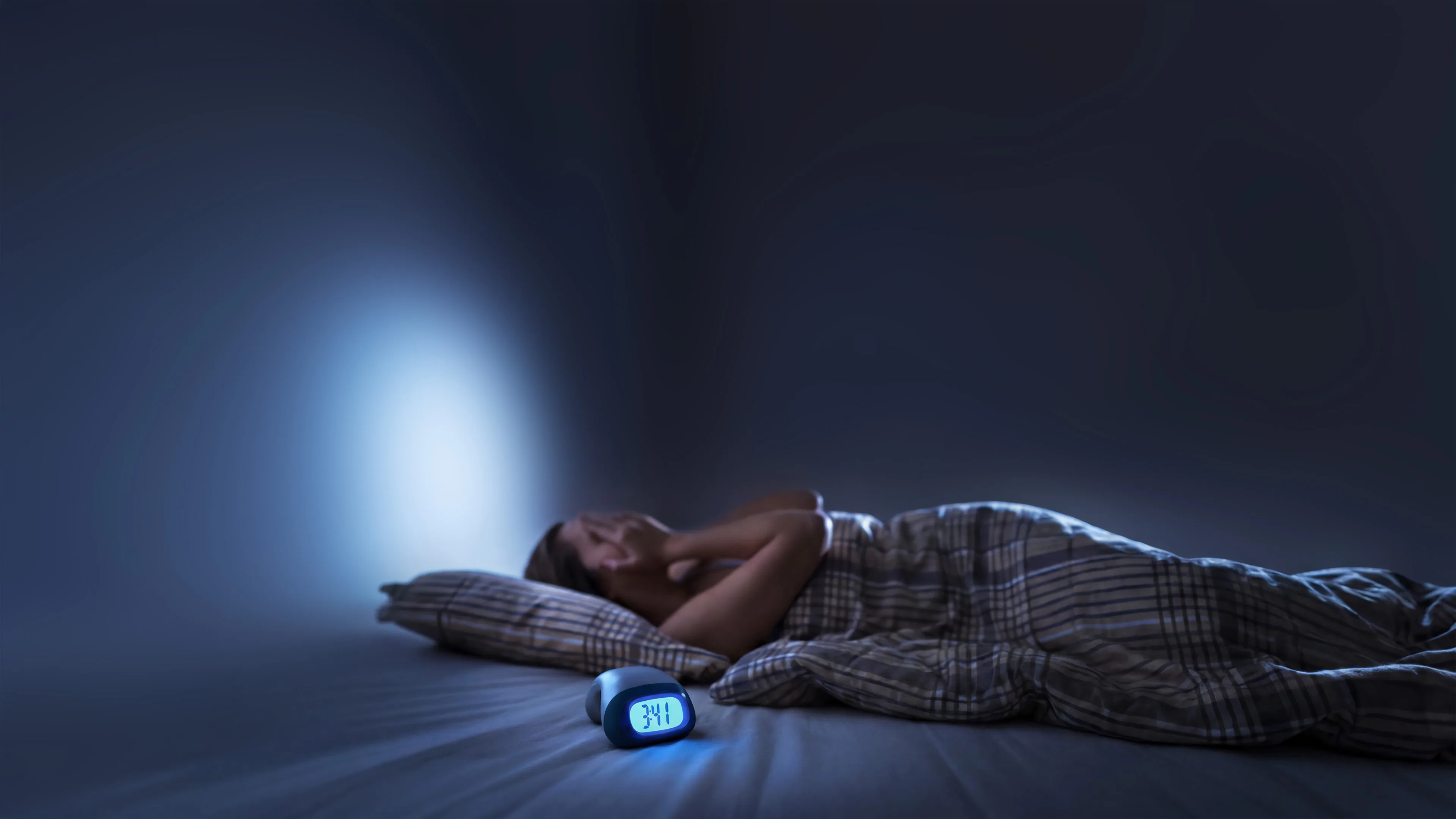 Person laying awake at night in their bed frustrated with an alarm clock beside them stating 3:41am