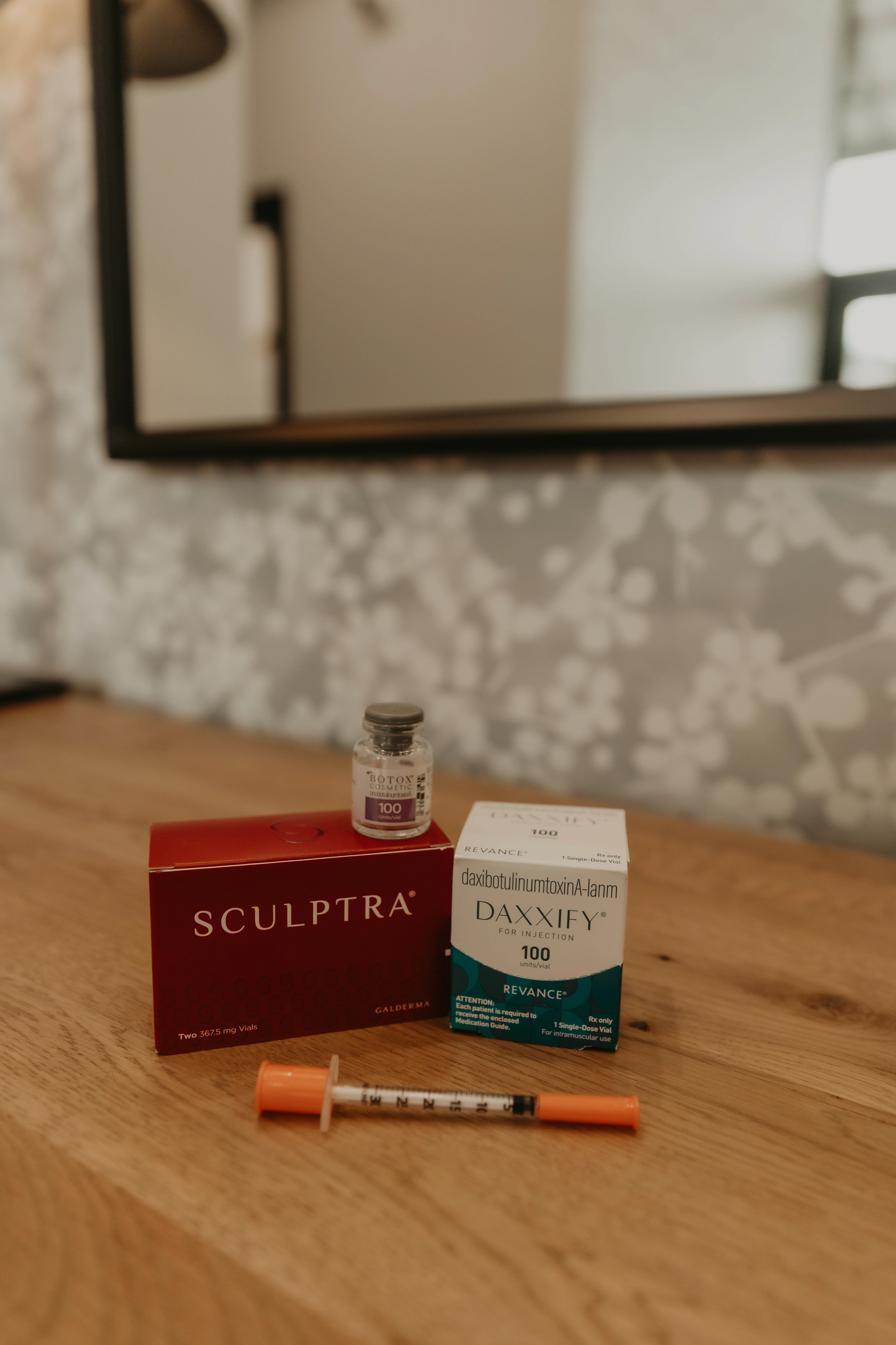 Vials of Sculptra and Daxxify cosmetic injectables with a syringe on a wooden surface.