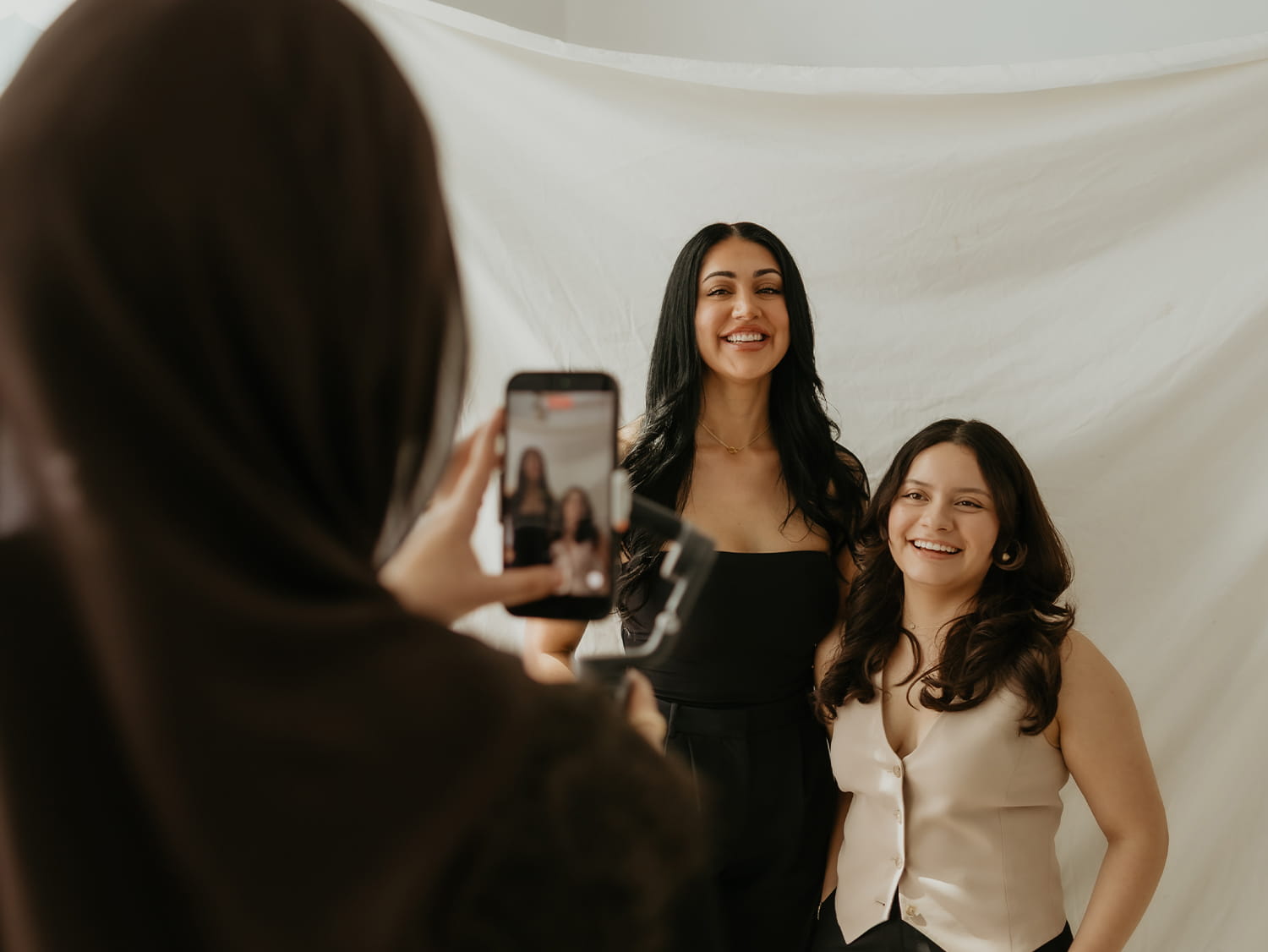 Four diverse women smiling and posing together in a bright room with wooden floors.