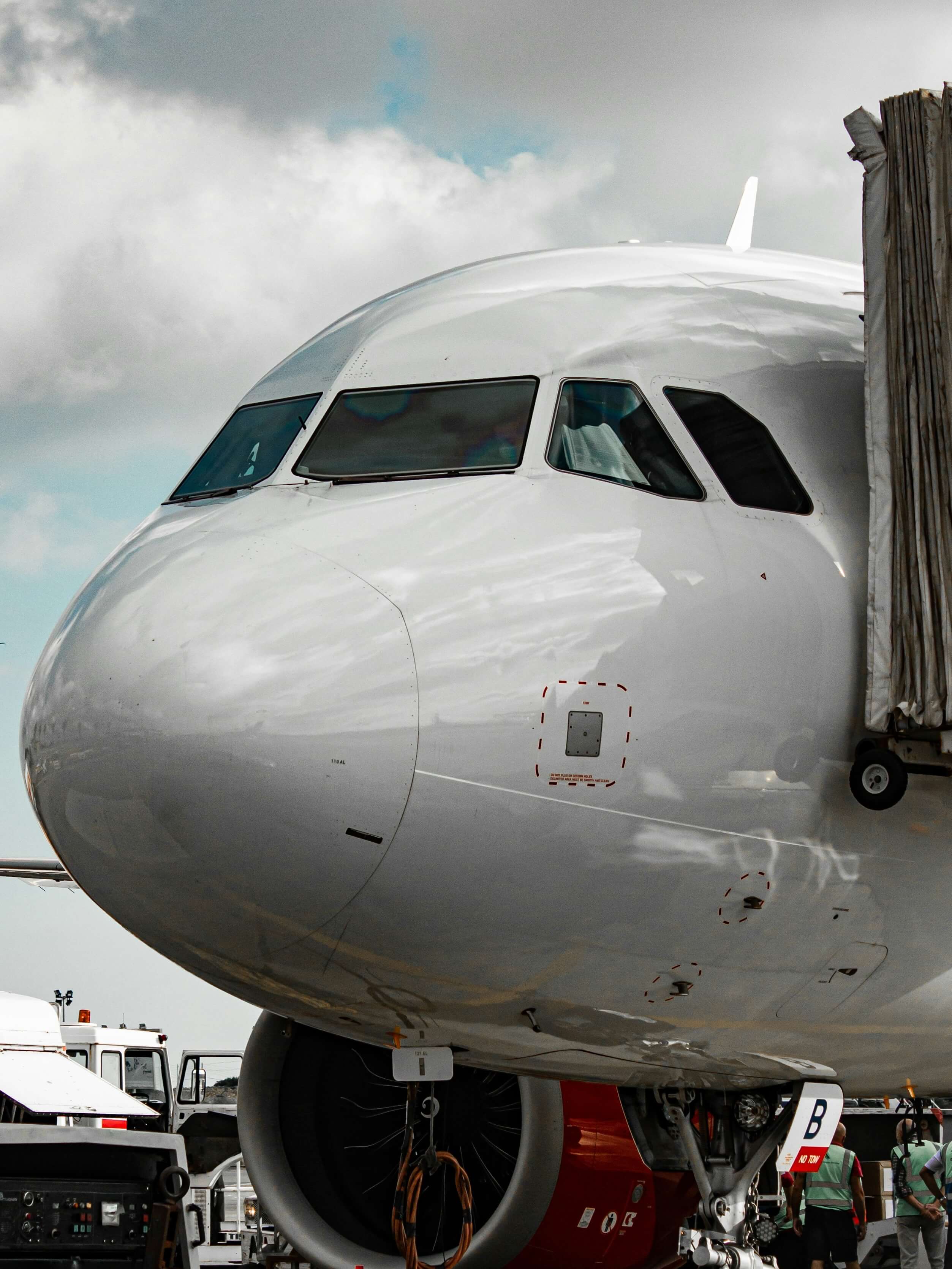 Close-up of a white airplane nose and cockpit at an airport with ground crew nearby.