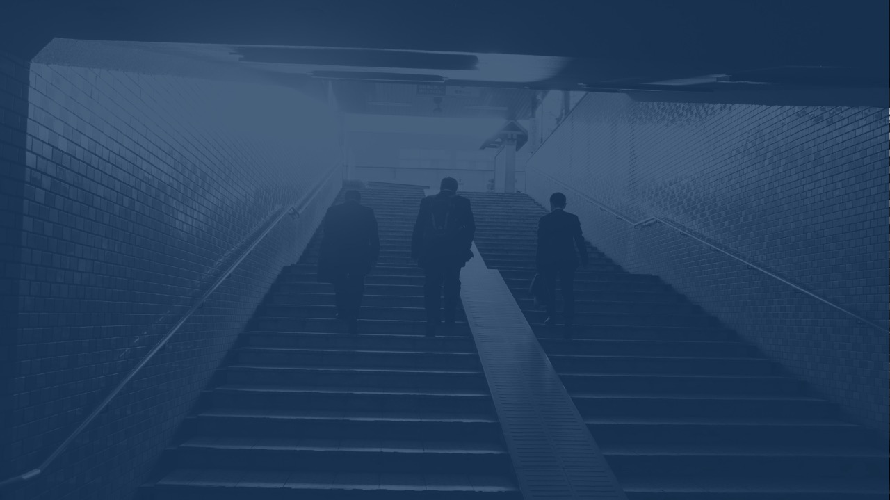 Three men in suits walking up stairs in a tiled subway or underground passage.