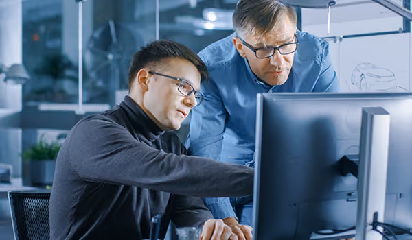 Two men wearing glasses working together and looking at a computer screen in an office.